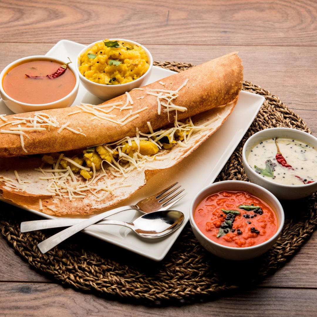Masala Dosa, un popular plato del sur de la India, servido en un plato blanco, relleno de papas especiadas y cubierto con queso rallado.